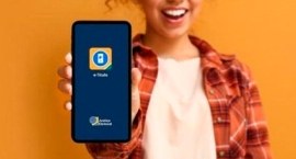 Pessoa sorrindo e segurando um smartphone com o aplicativo e-Título exibido na tela, em fundo la...