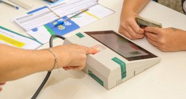 A imagem mostra o momento da coleta das digitais da eleitora durante o atendimento biométrico.