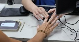 A imagem mostra o momento da coleta das digitais da eleitora durante o atendimento biométrico. A...