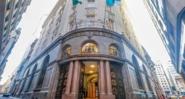 A imagem mostra um edifício histórico de esquina, com uma fachada imponente e detalhes arquitetô...