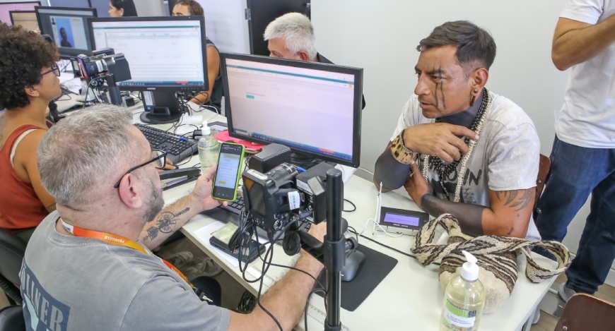 Um homem indígena, com pinturas no corpo, está sentado, durante o atendimento da Justiça Eleitor...