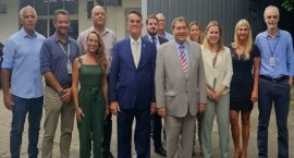 A imagem mostra um grupo de onze pessoas (sete homens e quatro mulheres) posando em frente ao pr...