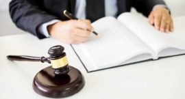 Em destaque, o martelo, que simboliza Justiça. Ao fundo, um homem de terno escreve em um livro