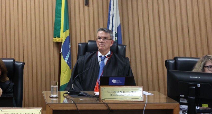 Foto do presidente do TRE-RJ, desembargador Claudio de Mello Tavares, sentado à mesa, sobre o qu...
