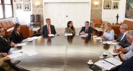 Grupo de 10 autoridades reunidas em torno de uma grande mesa redonda em sala institucional , ten...