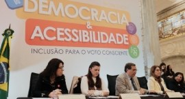 A mesa de abertura do evento com um painel  ao fundo "Workshop Democracia & Acessibilidade", com...