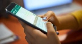 Uma pessoa segura um smartphone com as duas mãos e digita na tela, que exibe uma interface de co...