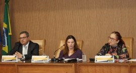 Mesa de autoridades do evento, realizado no auditório do TRE-RJ. Três pessoas estão sentadas lad...