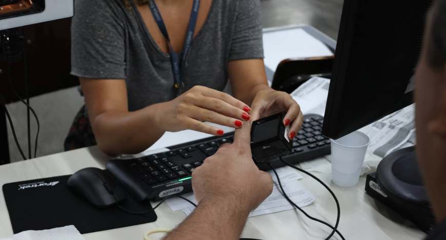 Uma servidora da Justiça Eleitoral colhe a biometria de um eleitor.
