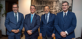 Quatro homens de terno e gravata posam lado a lado para uma foto, em ambiente interno, diante de...
