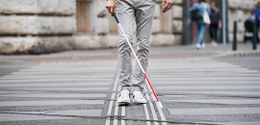 Foto de um homem andando na rua com uma bengala vermelha e branca