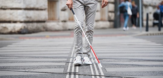 Foto de um homem andando na rua com uma bengala vermelha e branca