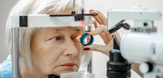 Descrição da imagem: Mulher idosa realizando exame oftalmológico em clínica, com equipamento de ...