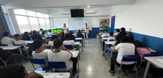 Duas mulheres estão em pé conduzindo uma palestra para um grupo de estudantes em uma sala de aula.