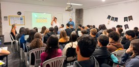Uma palestrante e um auxiliar conduzem uma palestra para estudantes sentados em uma sala, com a ...
