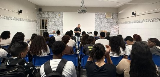 Em uma sala ampla e iluminada, quatro palestrantes de pé ao lado de bandeiras apresentam uma ati...