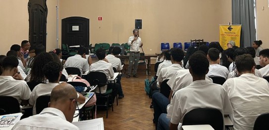 A imagem mostra uma apresentação do projeto "Eleitor do Futuro" em um auditório escolar. Um home...
