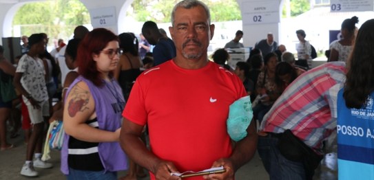 Jovem moreno, com cabelo curto e escuro, sorri ao lado da mãe, com cabelo longo. Eles posam tend...