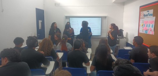 Duas mulheres estão em pé conduzindo uma palestra para um grupo de estudantes em uma sala de aula.