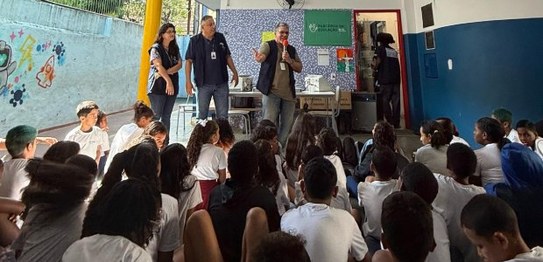 A imagem mostra um grupo de crianças sentadas no chão, vestindo uniformes escolares brancos, ass...