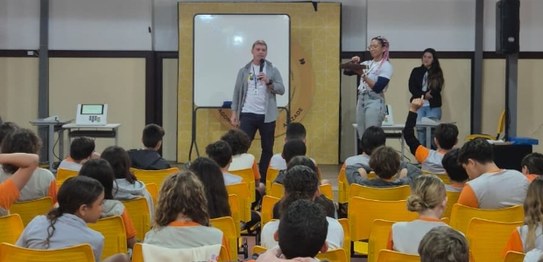 Duas mulheres estão em pé conduzindo uma palestra para um grupo de estudantes em uma sala de aula.