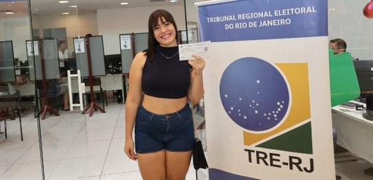 A imagem mostra a captura da digital de uma eleitora durante o cadastramento biométrico. O monit...