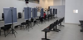 A imagem mostra o interior da Central de Atendimento ao Eleitor. À esquerda, há várias baias de ...