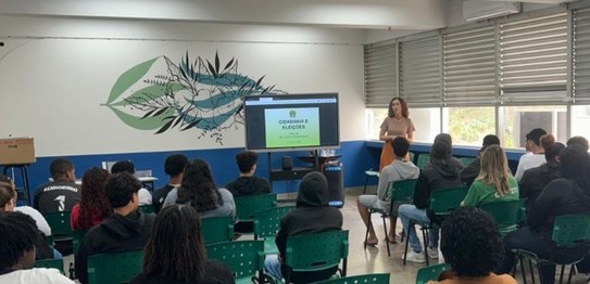 Turma de estudantes sentados em cadeiras verdes, assistindo a uma palestra conduzida por juíza. ...