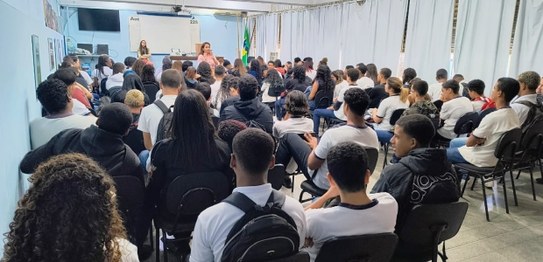 Descrição da imagem: O juiz veste um terno preto e segura um microfone em cima do palco. As(os) ...