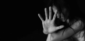 Imagem em preto e branco de uma mulher com expressão de sofrimento, levantando a mão aberta em d...