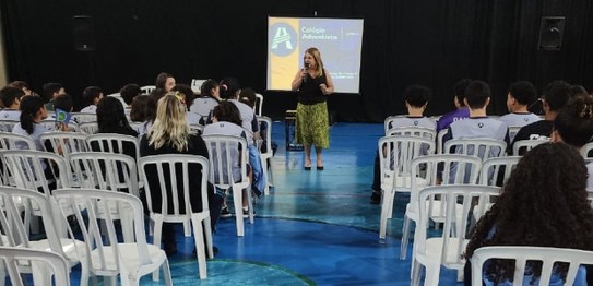 Descrição da imagem: O juiz veste um terno preto e segura um microfone em cima do palco. As(os) ...