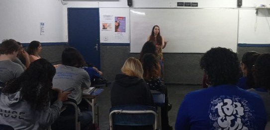 Descrição da imagem: Cinco alunos(as), três meninas e dois meninos, estão em pé e fazem fila par...