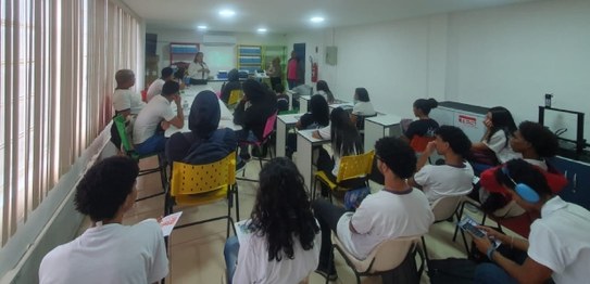Descrição da imagem: Cinco alunos(as), três meninas e dois meninos, estão em pé e fazem fila par...
