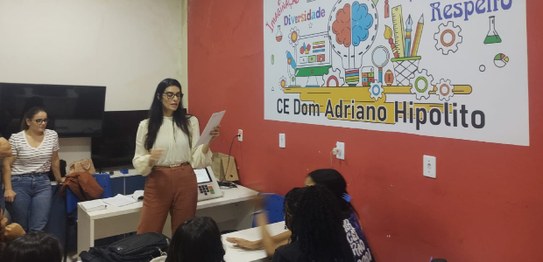 Descrição da imagem: Cinco alunos(as), três meninas e dois meninos, estão em pé e fazem fila par...