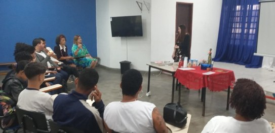 Descrição da imagem: Cinco alunos(as), três meninas e dois meninos, estão em pé e fazem fila par...