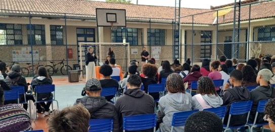 Turma de estudantes sentados em cadeiras verdes, assistindo a uma palestra conduzida por juíza. ...