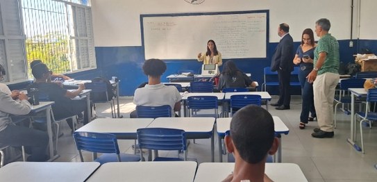 Descrição da imagem: O juiz veste um terno preto e segura um microfone em cima do palco. As(os) ...