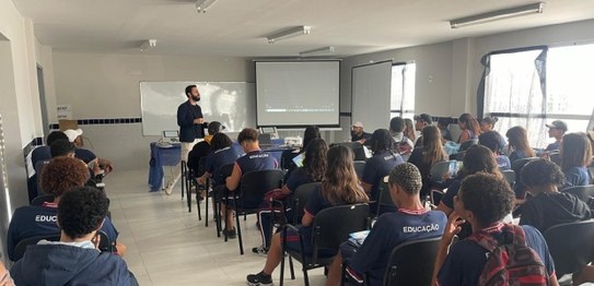Turma de estudantes sentados em cadeiras verdes, assistindo a uma palestra conduzida por juíza. ...