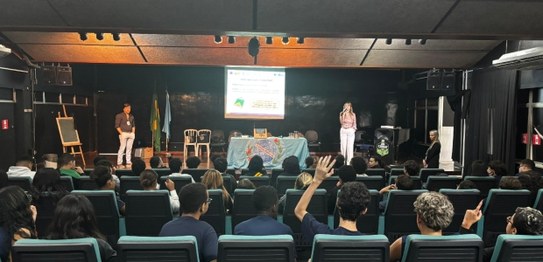 Turma de estudantes sentados em cadeiras verdes, assistindo a uma palestra conduzida por juíza. ...