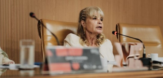 A imagem mostra uma mulher sentada em uma cadeira de couro marrom, em um ambiente que parece ser...