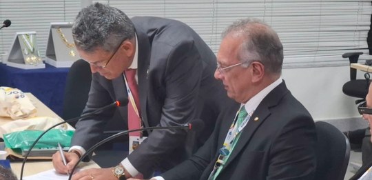 Presidente do TRE-RJ (à esq.) assina o termo de posse como 1º vice-presidente do Coptrel, ao lad...