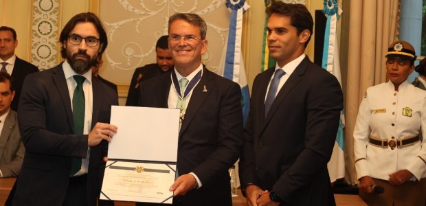 Desembargador Cláudio de Mello Tavares é homenageado pelo Tribunal de Contas do Rio Na imagem, o desembargador Cláudio de Mello Tavares aparece ao centro, sorrindo e segurando um d...