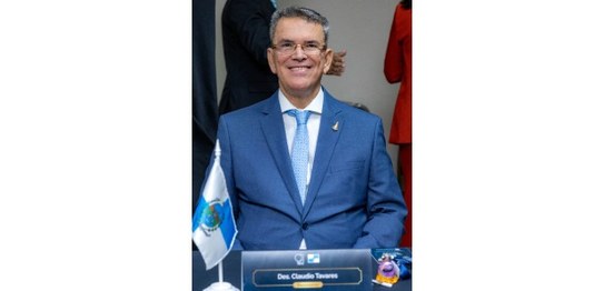O presidente do TRE-RJ aparece sentado à mesa do Coptrel, sorrindo para a câmera. Ele veste tern...