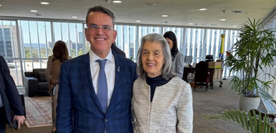 À esquerda, o desembargador Claudio Tavares está sorrindo de terno e óculos, ao lado da ministra...