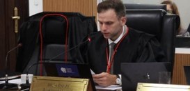 Desembargador eleitoral Bruno Bodart sentado, olhando para baixo, realizando um discurso.