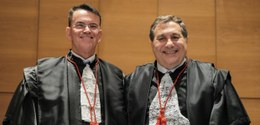 A imagem mostra dois homens vestidos com trajes formais de magistrados, incluindo togas pretas e...