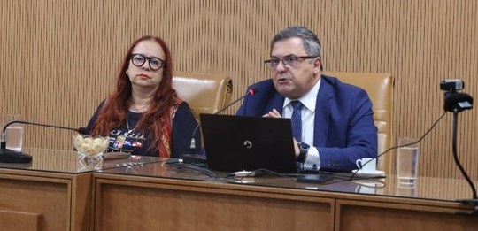 A professora Vânia Aieta (à esquerda), ruiva e de óculos, está sentada ao lado do desembargador ...