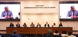 Mesa de autoridades em um auditório, com oito pessoas sentadas participando de um evento ou pale...
