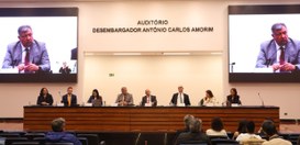 Mesa de autoridades em um auditório, com oito pessoas sentadas participando de um evento ou pale...