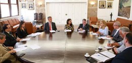 Grupo de 10 autoridades reunidas em torno de uma grande mesa redonda em sala institucional , ten...